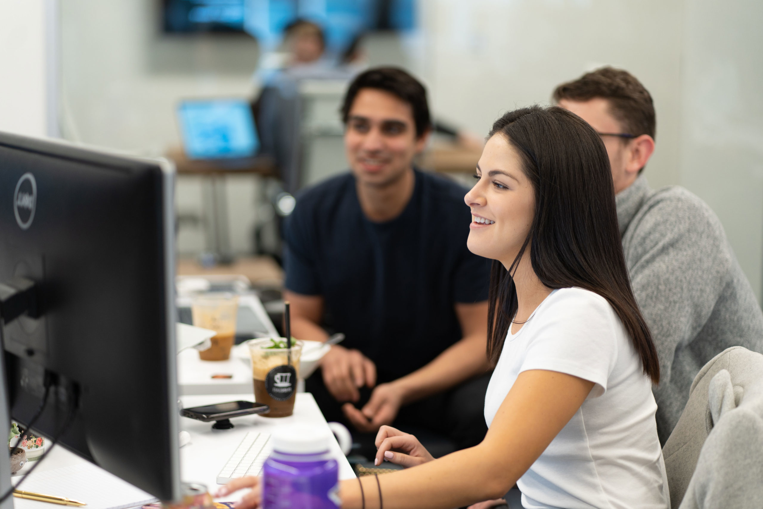 Photograph of three teammates looking at a desktop computer and smiling.